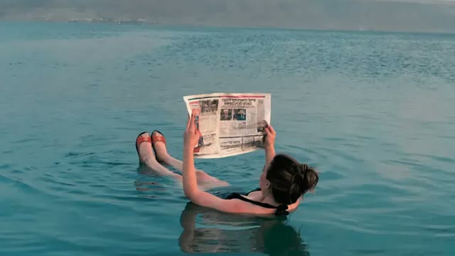 Woman floating in a calm turquoise sea reading a newspaper